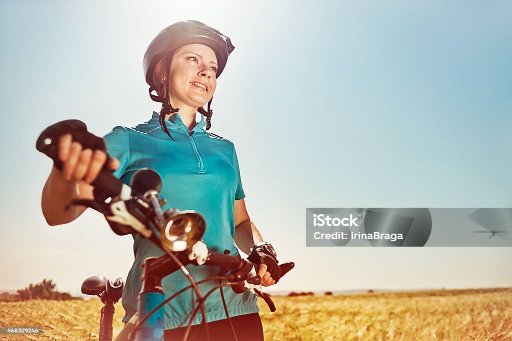 Beautiful woman with a bike on a field looking around Beautiful young woman with a bike on a field looking around 2015 Stock Photo