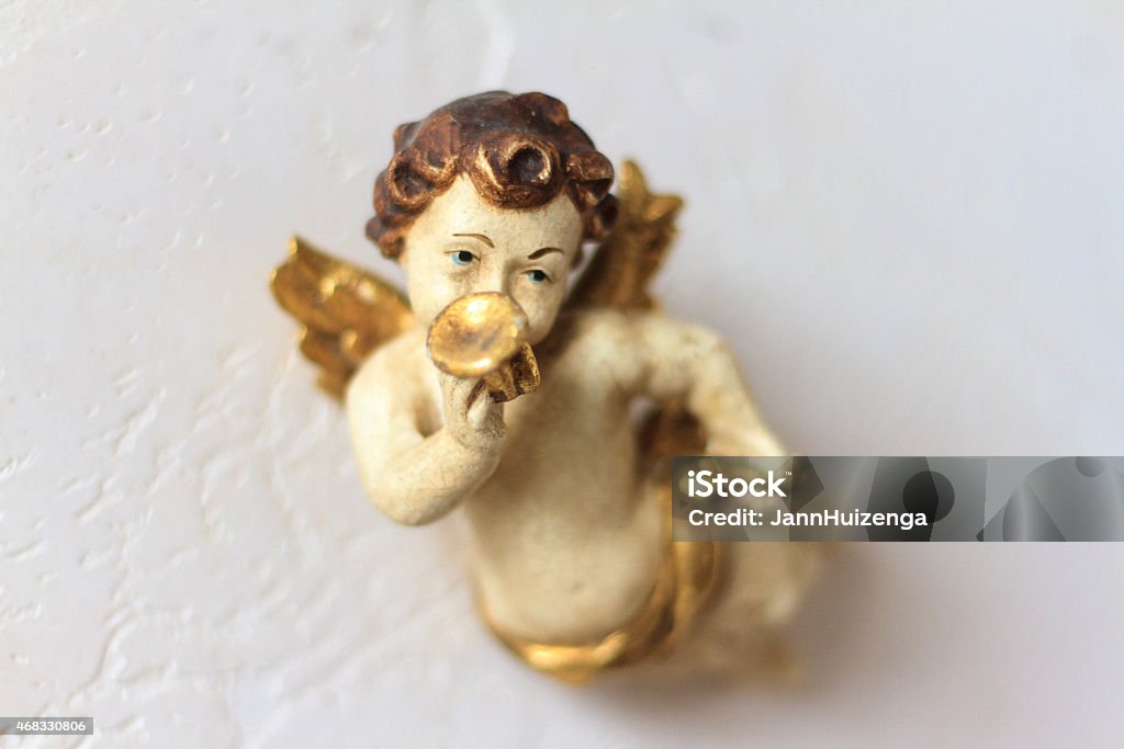 Sweet Antique Wood Cherub-Angel With Gold Trumpet A 19th-century wooden cherub-angel with gold wings playing a gold trumpet, made by an unknown sculptor in Sicily. Sharp focus on trumpet and eyes with soft focus elsewhere and plenty of copy space on the white wall background. Trumpet Stock Photo