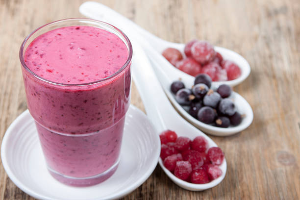  Smoothies from the berries of black and red currants, gooseberries and yogurt in a glass on a wooden table variegated brown table. And berries in white spoons next. 