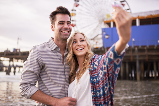 romantic couple taking selfies together in santa monica with smartphone and shot in horizontal composition