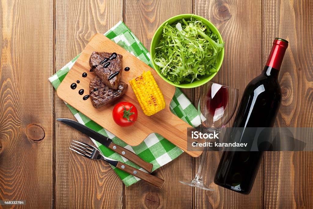 Steak with grilled corn, salad and red wine Steak with grilled corn, salad and red wine over wooden table. Top view 2015 Stock Photo