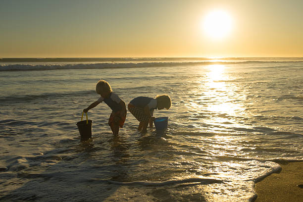 Happy children playing with sand at the beach together in summer at sunset