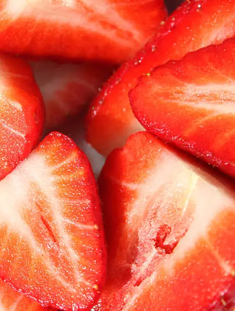 Photo showing a white, square dish filled with sliced strawberries.  These fresh strawberries are particularly red, perfectly ripe and juicy.  They are homegrown and have just been picked, being sliced in half, ready to be covered in cream and sugar, as a traditional summer dessert with some noteworthy health benefits.