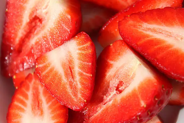 Photo showing a white, square dish filled with sliced strawberries.  These fresh strawberries are particularly red, perfectly ripe and juicy.  They are homegrown and have just been picked, being sliced in half, ready to be covered in cream and sugar, as a traditional summer dessert with some noteworthy health benefits.