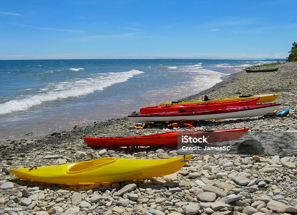 Kayaks on the beach Four colorful Kayaks on a rocky beach with blue water, waves and blue sky with slight traces of cloud. Summer in Ontario, Canada on the shore of Georgian Bay Kayak Stock Photo