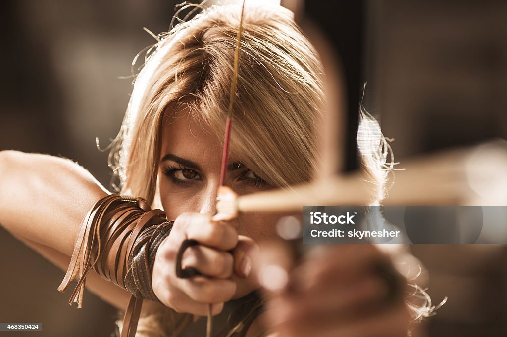Woman archer aiming with bow and arrow. Close-up of mid adult woman aiming with bow and arrow. Archery Stock Photo