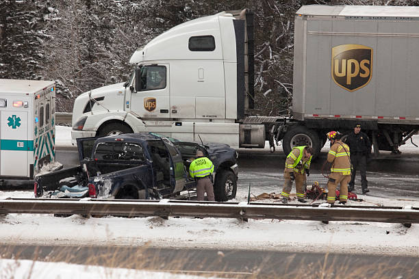 Georgetown, Colorado, USA - February 6, 2014: On a snowy day with icy driving conditions on westbound Interstate 70, a state trooper and fire fighters with emergency vehicles attend to a crashed pickup truck near the guardrail on the slick highway as UPS semi-truck passes on the far right lane.