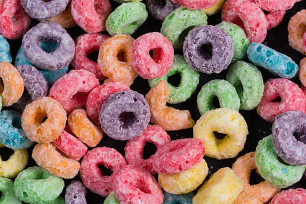 Fruit O shaped cereal, loops, with lots of color scattered over a black background.  Pink, purple, orange, green, yellow, blue contrast nice against the black.  Great for posters, signs, wallpapers and more in a background.