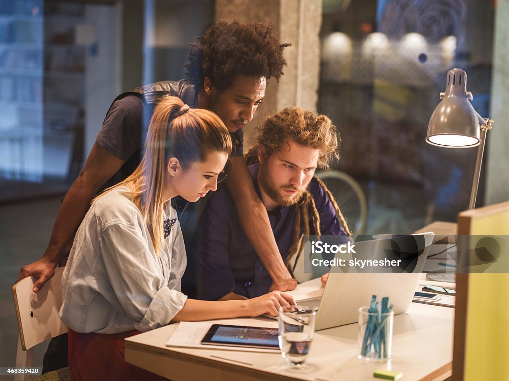 Creative team using computer in the office. Three young designers using laptop on a meeting. The view is through the glass. 2015 Stock Photo