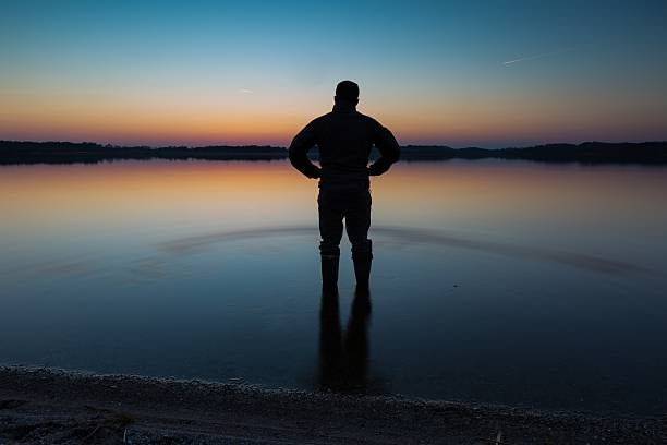 istock Man standing in lake water at sunset 468359534