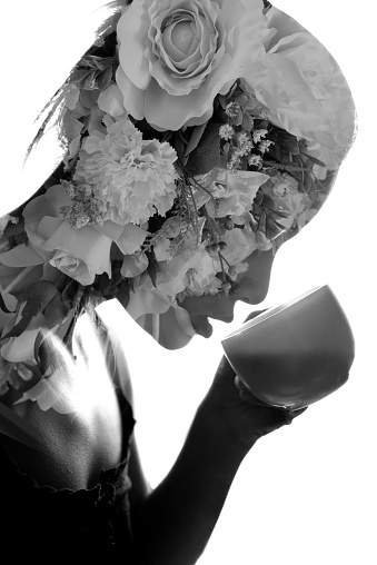 Double exposure of bouquet and young woman in black dress drinking white cup of tea on white background.
