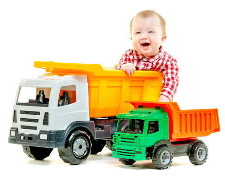 Funny toddler sitting in the back of a large toy truck. Isolated on white