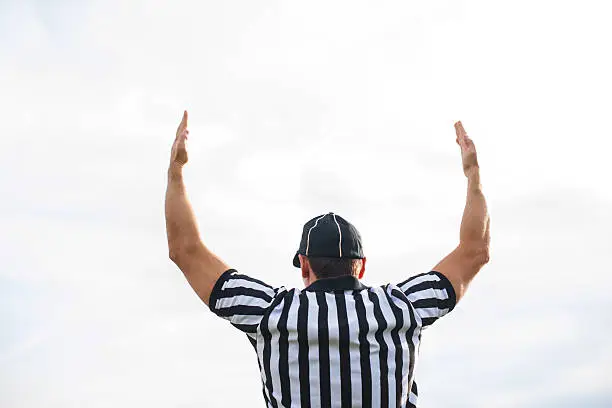 Rear view of American football judge shoving touchdown against the sky.