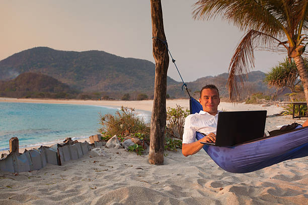 man uses laptop remotely at the beach