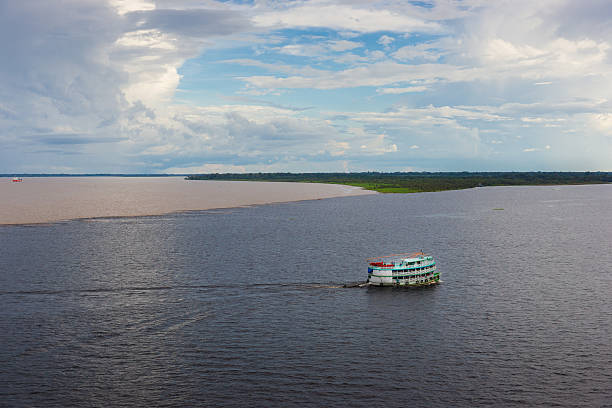 Meeting of Waters Rio Negro Meets Solimões and Forms Amazon The Meeting of Waters is the confluence between the Rio Negro, a river with dark full of tannins water, and the sandy-colored Amazon River or Rio Solimões, as it is known the upper section of the Amazon in Brazil. For 6 km (3.7 mi) the river's waters run side by side without mixing. The same also happens near Santarém, Pará with the Amazon and Tapajós rivers. rio negro brazil stock pictures, royalty-free photos & images