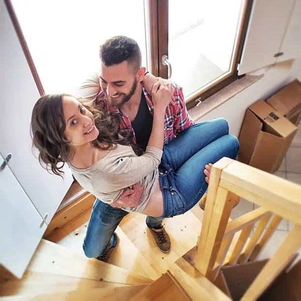 Photo of You man carrying his wife upstairs in their new house