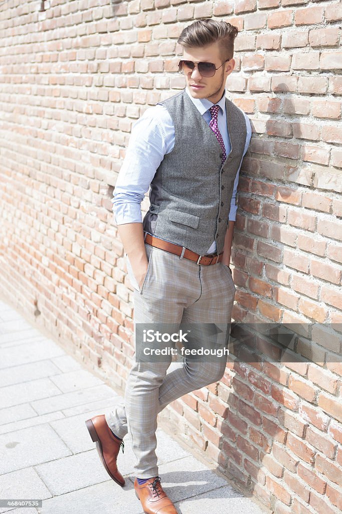 casual man leans on a brick wall casual young man leaning on a brick wall with his hands in his pockets while looking away from the camera Adult Stock Photo