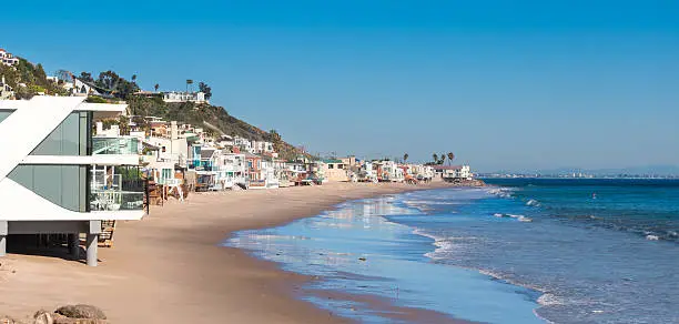 Beach with row of luxury homes facing the Pacific Ocean in Malibu, California, USA on a clear blue sky day.