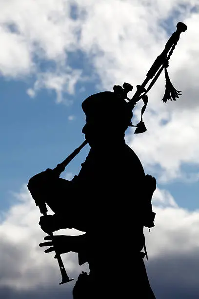 A man playing the bagpipes, silhouetted against clouds in the sky