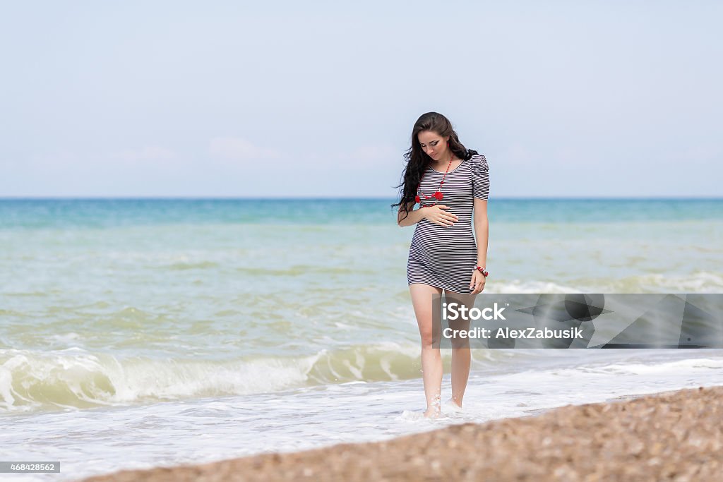 Expectant mother on the beach Expectant mother on the beach. Pregnant woman in striped dress walking along the seashore Pregnant Stock Photo