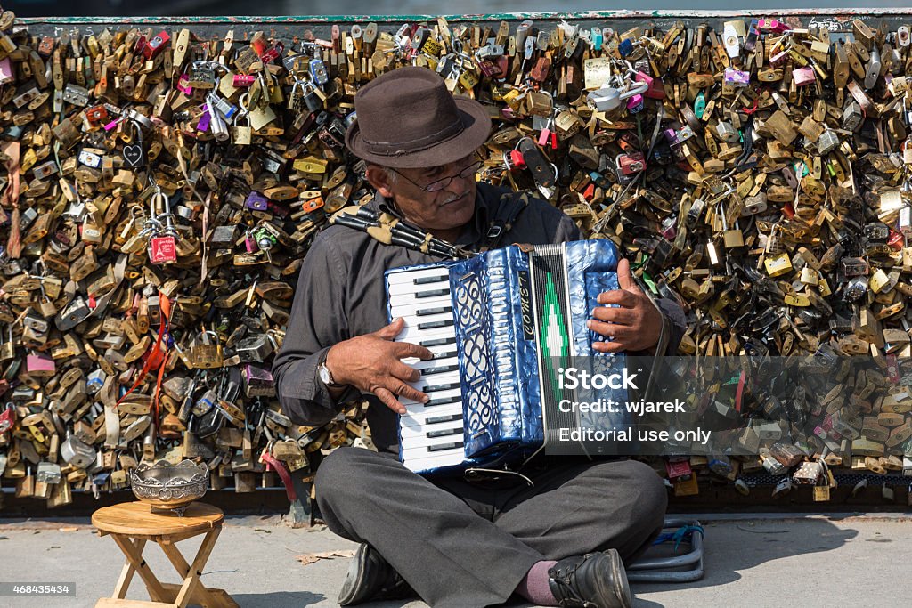 Paris Paris, France - September 8, 2014: - Pont de l'Archeveche (Archbishop's Bridge) An accordion player sitting on a bridge in Paris and plays French songs. Behind him is the bridge railing, full of thousands of love locks.  2015 Stock Photo