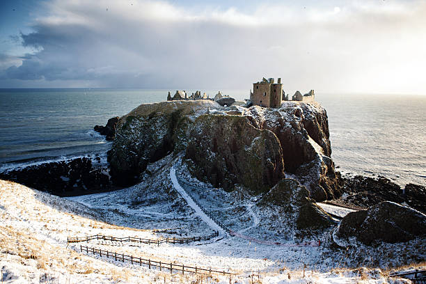 Horizontal View in Snow - Dunnottar Castle, Stonehaven, Scotland UK Dunnottar Castle is a ruined medieval fortress located upon a rocky headland on the north-east coast of Scotland, about 3 kilometers (1.9 mi) south of Stonehaven. The surviving buildings are largely of the 15th and 16th centuries, but the site is believed to have been fortified in the Early Middle Ages. Dunnottar has played a prominent role in the history of Scotland through to the 18th-century Jacobite risings because of its strategic location and the strength of its situation. Dunnottar is best known as the place where the Honours of Scotland, the Scottish crown jewels, were hidden from Oliver Cromwell's invading army in the 17th century. The property of the Keiths from the 14th century, and the seat of the Earl Marischal, Dunnottar declined after the last Earl forfeited his titles by taking part in the Jacobite rebellion of 1715. The castle was restored in the 20th century and is now open to the public. headland photos stock pictures, royalty-free photos & images