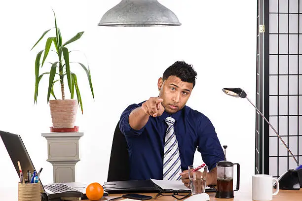 An image of an Indian office worker with a blue shirt behind his desk