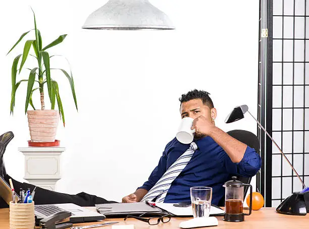 An image of an Indian office worker with a blue shirt behind his desk