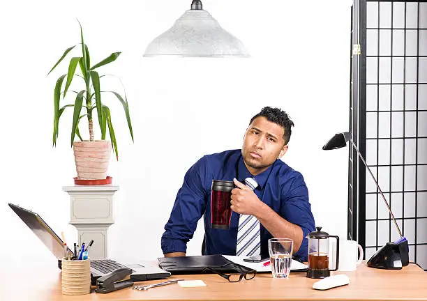 An image of an Indian office worker with a blue shirt behind his desk