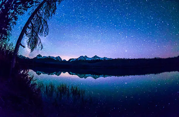 Beautiful Little Redfish Lake at night with Sawtooth mountains in the background and star filled sky reflecting in the background. Picture taken with Nikon 16 mm fish-eye lens