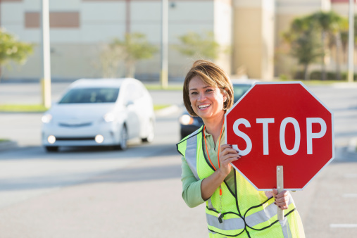 School crossing guard:  Hispanic woman (50s) standing at crosswalk with stop sign.