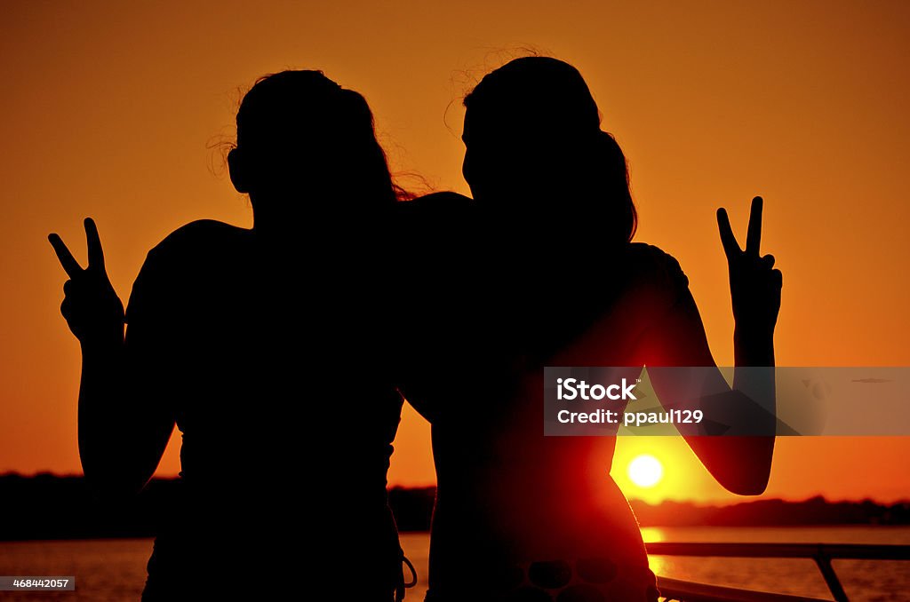 Deux filles donner signe de la paix au coucher du soleil au bord de l'océan - Photo de Adolescent libre de droits