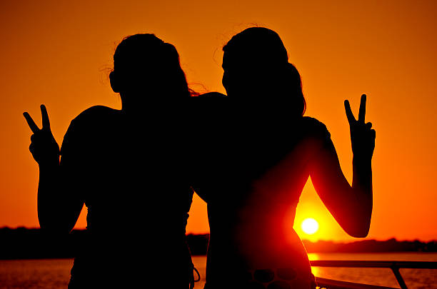Two Girls Giving Peace Sign at Sunset by the Ocean stock photo