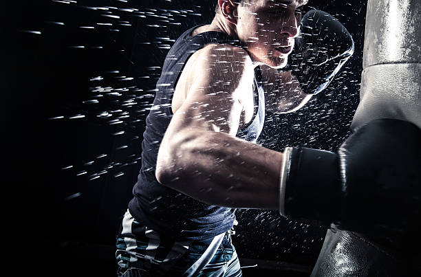istock Sweating boxer punching a black bag on black background 468442806