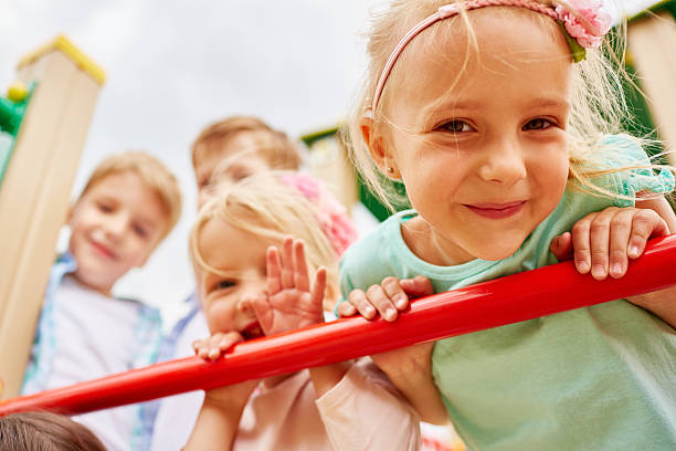 Climbing jungle gym ladder Charming little girl leaning on jungle gym ladder surrounded by her friends girl climbing ladder stock pictures, royalty-free photos & images