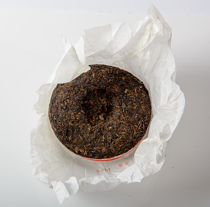 Disc of chinese puer tea in  unwrapped packing on green background
