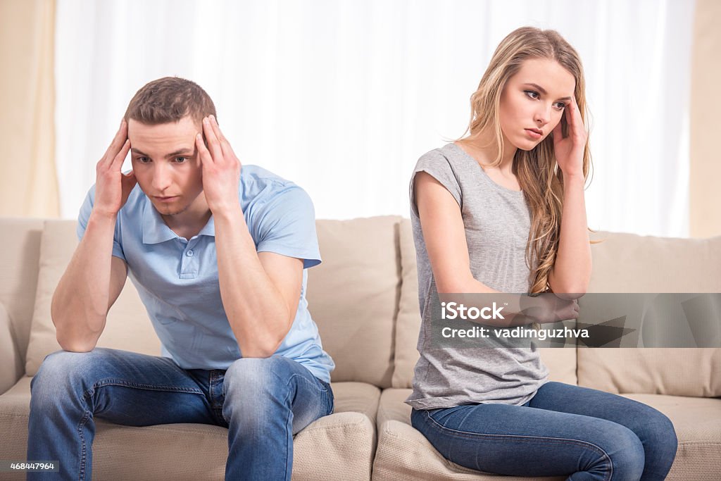 Problems in relationships Relationship difficulties. Depressed young man and woman sitting close to each other on the couch and holding head in hands. 2015 Stock Photo