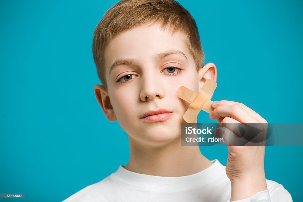 Boy tearing off adhesive plaster from his cheek Portrait of a boy with tearing off adhesive plaster from his cheek 2015 Stock Photo