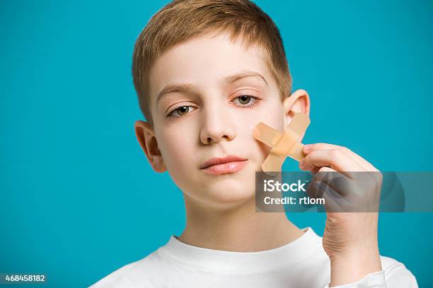 Boy Tearing Off Adhesive Plaster From His Cheek Stock Photo - Download Image Now - 2015, Adhesive Bandage, Adhesive Tape