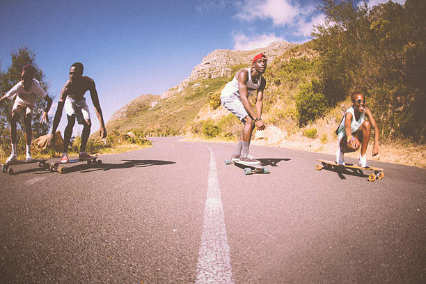 gemischte ethnische gruppe von teen skateboarder racing downhill zusammen - longboard skating stock-fotos und bilder