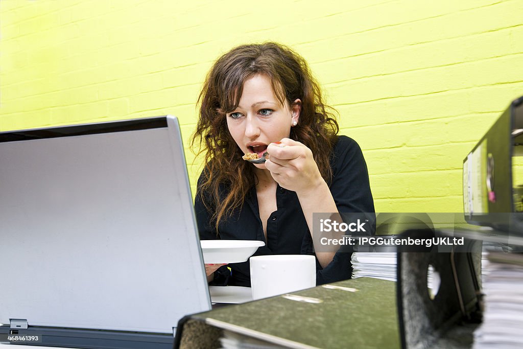 Caucasiana Jovem mulher comendo e trabalhando em sua mesa - Foto de stock de 20 Anos royalty-free