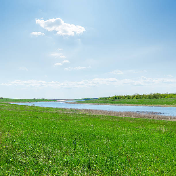 river in green grass and clouds over it