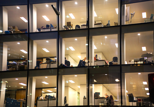 London, UK - December 19, 2014: Office block with lots of lit up windows and late office workers inside. City of London business aria in dusk.