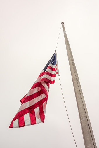 Half mast American flag concept as a symbol of the United States flying at low level to honor respect and mourning for fallen heroes.