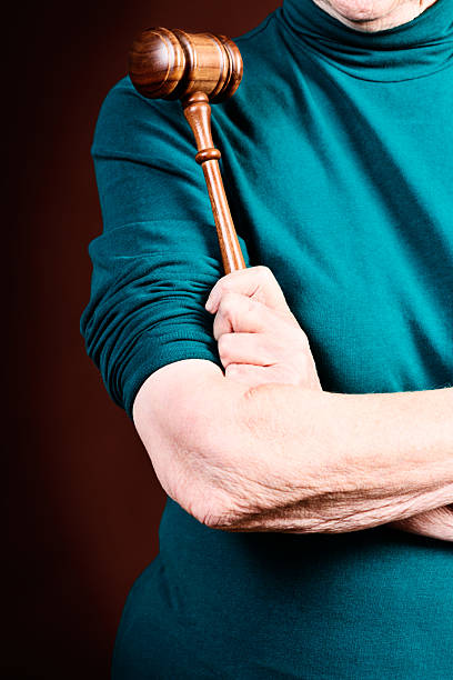 istock Judgement Day: old woman with folded arms holds judge's gavel 468476873