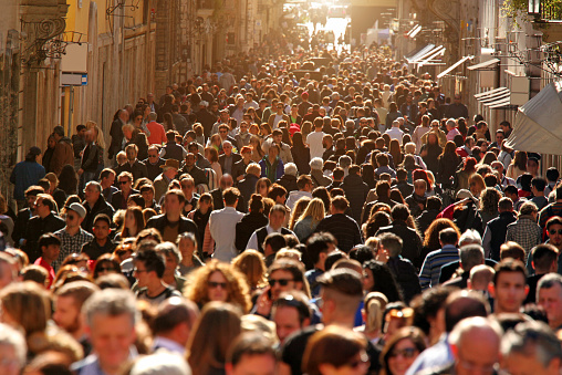 Large group of people crowding Rome's downtown streets in a sunny day. On a warm day the historic downtown of Rome, Italy, is flooded by people and tourists enjoying monuments and famous places. Horizontal composition.