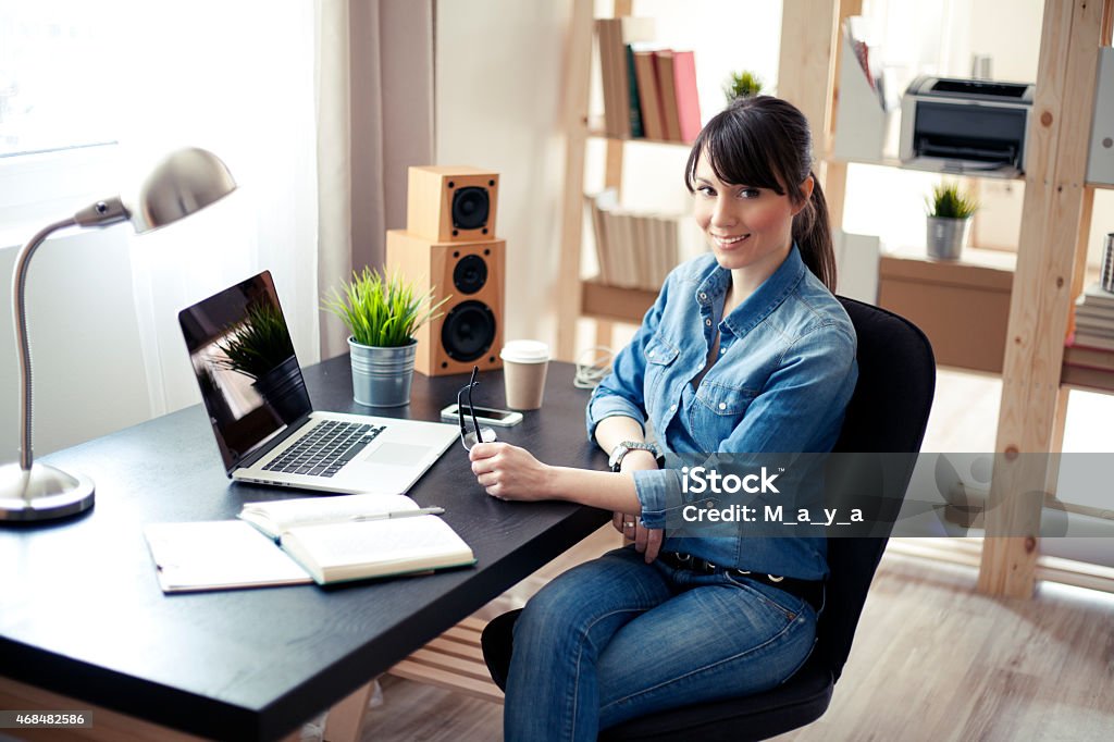 Women at modern home office. Young beautiful woman working at her home office. Office consists of wooden shelves and modern wooden table. 2015 Stock Photo