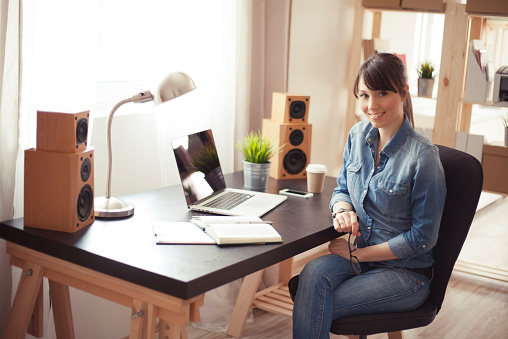 Young beautiful woman working at her home office. Office consists of wooden shelves and modern wooden table.