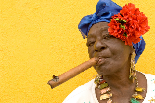 Havana, Cuba-February 12, 2008. A Cuban woman, smoking a large cigar, in colorful colonial costume near the Plaza de la Catedral in the old quarter of Havana