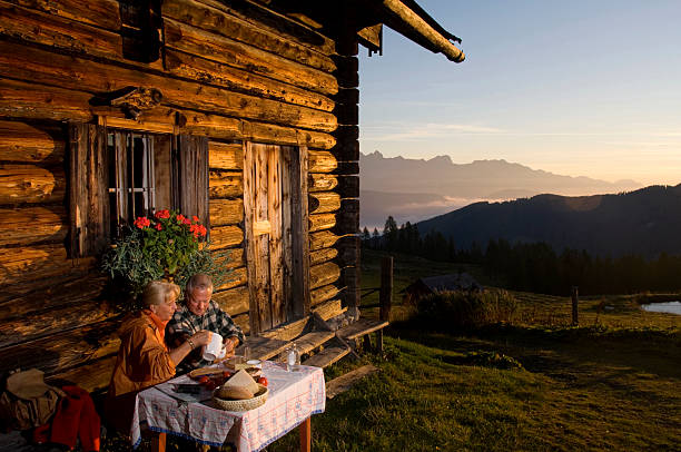 couple d'âge mûr assis en face de cabine de montagne, tout en regardant le coucher de soleil - autumn table setting flower photos et images de collection